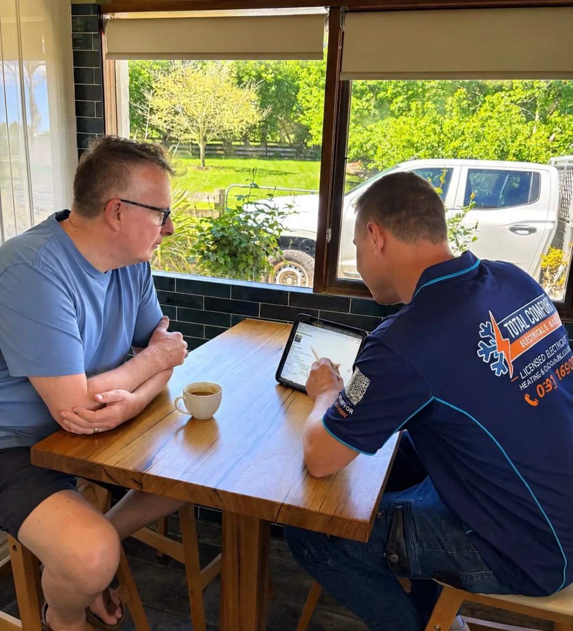 Total Comfort electrician going through the options on a tablet with a customer at their kitchen table