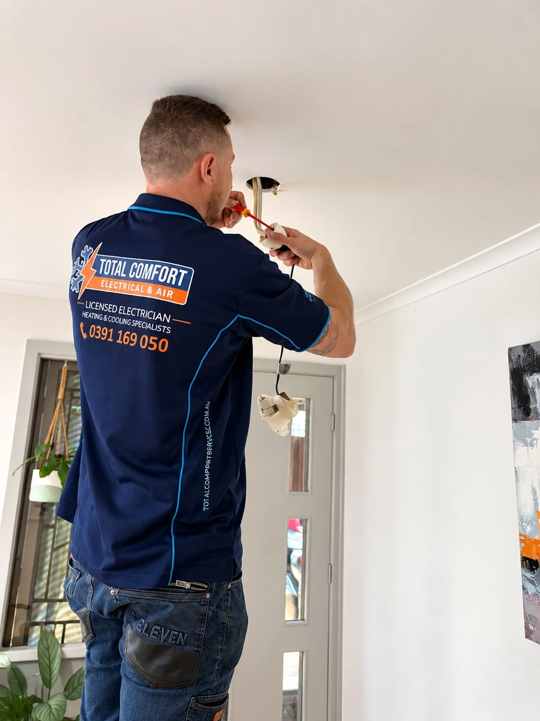 Total Comfort electrician working on a ceiling light fitting